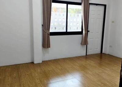 Empty bedroom with wooden flooring, a window with curtains, and a door.