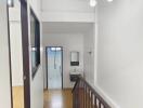 Interior hallway with staircase, leading to a bathroom, featuring wooden floors, white walls, and a modern light fixture