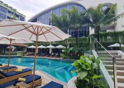 Luxury outdoor pool area with sun loungers, umbrellas, and tropical plants in modern resort