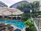 Luxury outdoor pool area with sun loungers, umbrellas, and tropical plants in modern resort