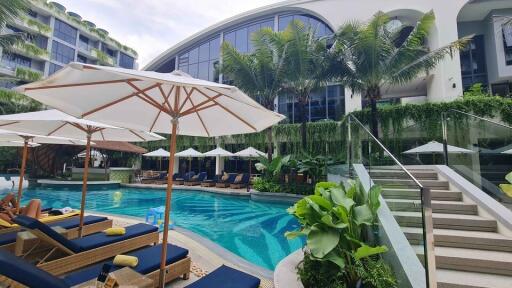 Luxury outdoor pool area with sun loungers, umbrellas, and tropical plants in modern resort