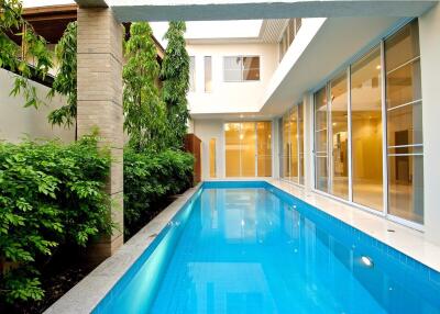 View of outdoor swimming pool with adjacent building and greenery