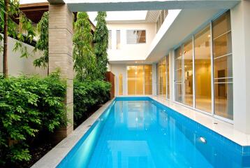 View of outdoor swimming pool with adjacent building and greenery