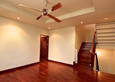 Spacious living room with hardwood floors, ceiling fan, and staircase
