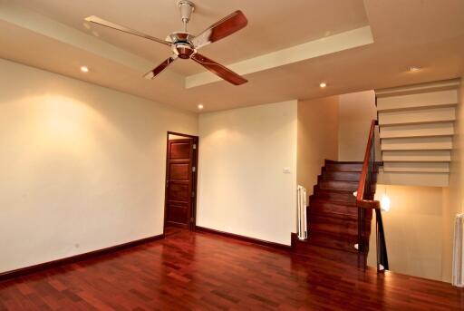 Spacious living room with hardwood floors, ceiling fan, and staircase