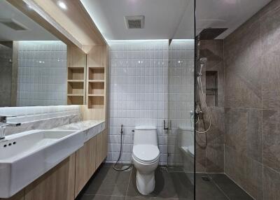 Modern bathroom with white and grey tiles, glass shower, and long vanity mirror.