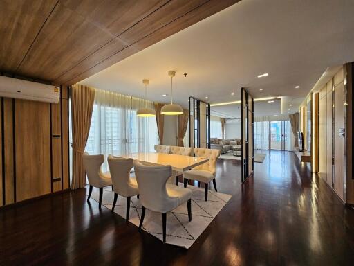 Modern dining room with wooden ceiling, white chairs and a table, connected to a spacious living area