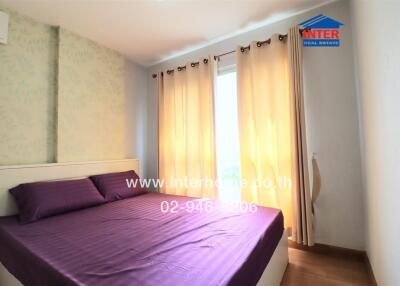 Bedroom with a double bed, purple bedding, and large windows with beige curtains.