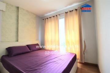 Bedroom with a double bed, purple bedding, and large windows with beige curtains.