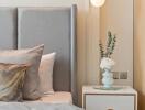 Modern bedroom with a gray upholstered headboard and a bedside table with a lamp and floral decoration