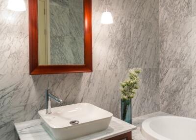 Modern bathroom with marble walls, sink, mirror, and bathtub