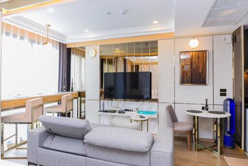 Modern living room with a mounted TV, a gray sofa, dining area, and a wall of windows.