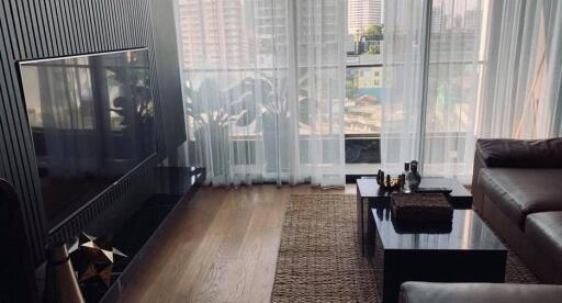 Modern living room with floor-to-ceiling windows, a sleek sectional sofa, wooden floors, and a view of the city.