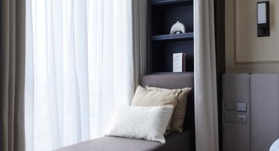 A cozy bedroom with curtains, shelves, and pillows