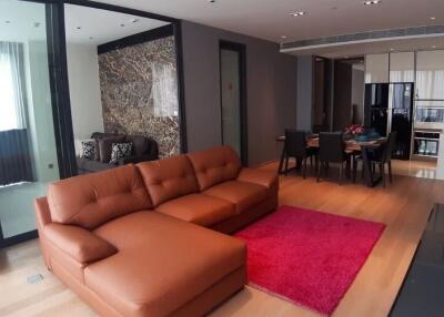 Modern living room with an open kitchen, featuring a brown sectional sofa, red rug, open dining area, and stylish decor