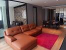 Modern living room with an open kitchen, featuring a brown sectional sofa, red rug, open dining area, and stylish decor