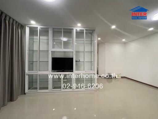 Modern living room with built-in white cabinetry and glass doors, featuring a TV and tiled flooring.