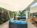 Modern outdoor seating area with blue cushions, covered patio, and greenery