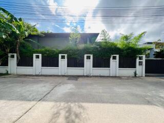 Exterior view of a modern residence with lush greenery and a gated fence