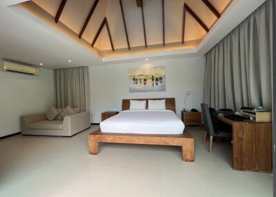 Spacious bedroom with a modern design, featuring a unique ceiling, comfortable bed, sofa, and work area