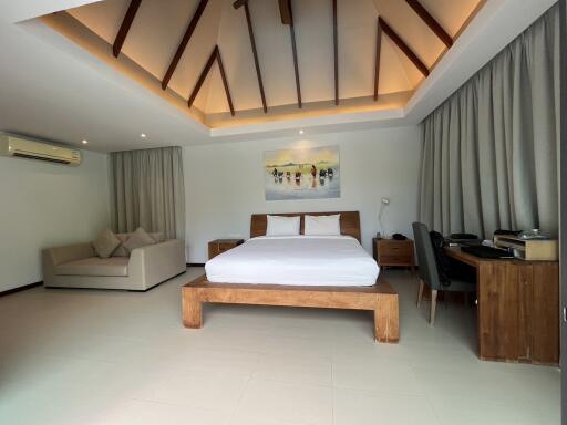 Spacious bedroom with a modern design, featuring a unique ceiling, comfortable bed, sofa, and work area