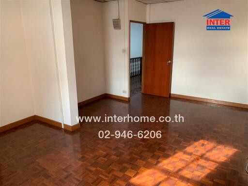 Bedroom with wooden flooring, white walls, and a door leading to another room