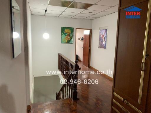 Hallway with stairs and wooden railing, hanging light fixture, and wall decorations