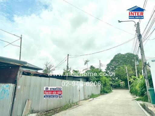 Street view showing a fenced property with real estate signage and surrounding greenery