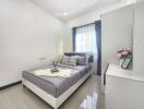 Modern bedroom with gray bedding, white walls, and natural light.