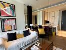 Modern living room with a white sofa, colorful wall art, and a view of the adjacent kitchen.