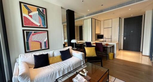 Modern living room with a white sofa, colorful wall art, and a view of the adjacent kitchen.