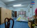 Simple bedroom with blue tiled floor, basic furniture, and a large window.