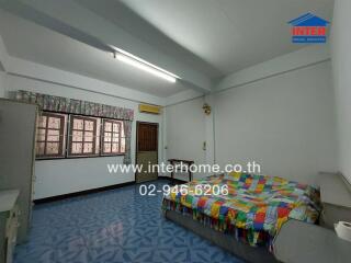 Bedroom with colorful bedspread, windows, air conditioning unit, and patterned blue flooring.