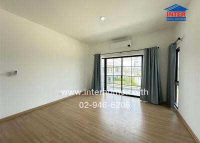Spacious bedroom with wooden flooring, large windows, and air conditioning unit.