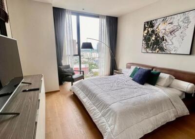 Modern bedroom with a large bed and a flat-screen TV, featuring artwork and city views
