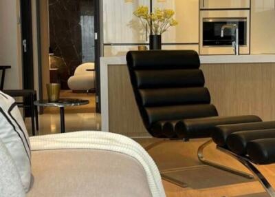 Modern living room with black leather chair, sofa, and view into kitchen area.