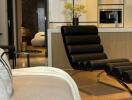 Modern living room with black leather chair, sofa, and view into kitchen area.