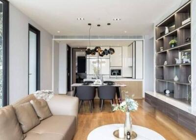 Modern living room with a view of dining area and kitchen, featuring stylish hanging lights and wooden flooring.