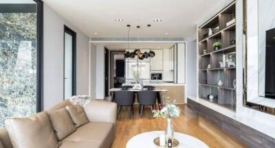 Modern living room with a view of dining area and kitchen, featuring stylish hanging lights and wooden flooring.