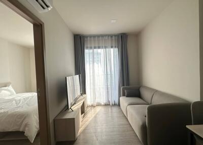 Modern living room with a grey sofa, TV, large window and bedroom entrance