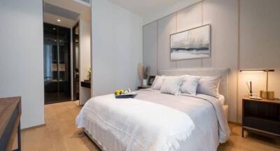 Modern bedroom with a neatly made bed, wooden flooring, and a bedside table with a lamp