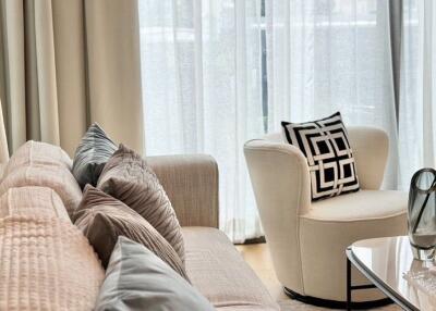 Modern living room with beige couch, decorative pillows, armchair, and glass vase on coffee table