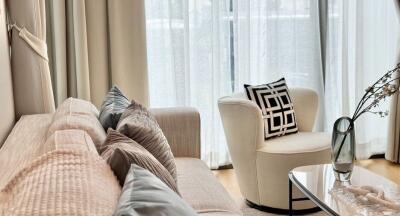 Modern living room with beige couch, decorative pillows, armchair, and glass vase on coffee table