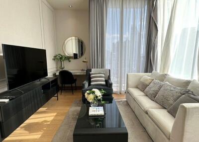 Bright and modern living room with a large window, a comfortable sofa, a black TV unit, a coffee table with flowers, and a workspace area.