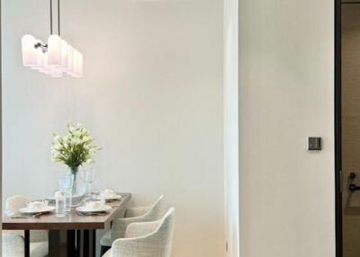 A modern dining area with a table set for four, white chairs, a floral centerpiece, and a wall-mounted light fixture.