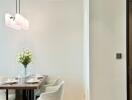 A modern dining area with a table set for four, white chairs, a floral centerpiece, and a wall-mounted light fixture.