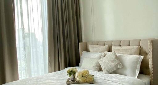 Well-lit bedroom with neatly made bed, decorative pillows, and tray with flowers