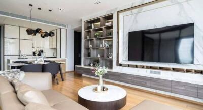 Modern living room with wall-mounted TV, open kitchen, and stylish shelving unit