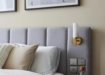 Modern bedroom with grey upholstered headboard, pillows, sconce lighting, and wall art