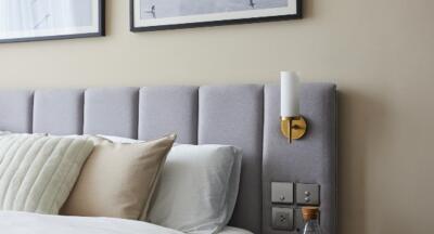 Modern bedroom with grey upholstered headboard, pillows, sconce lighting, and wall art